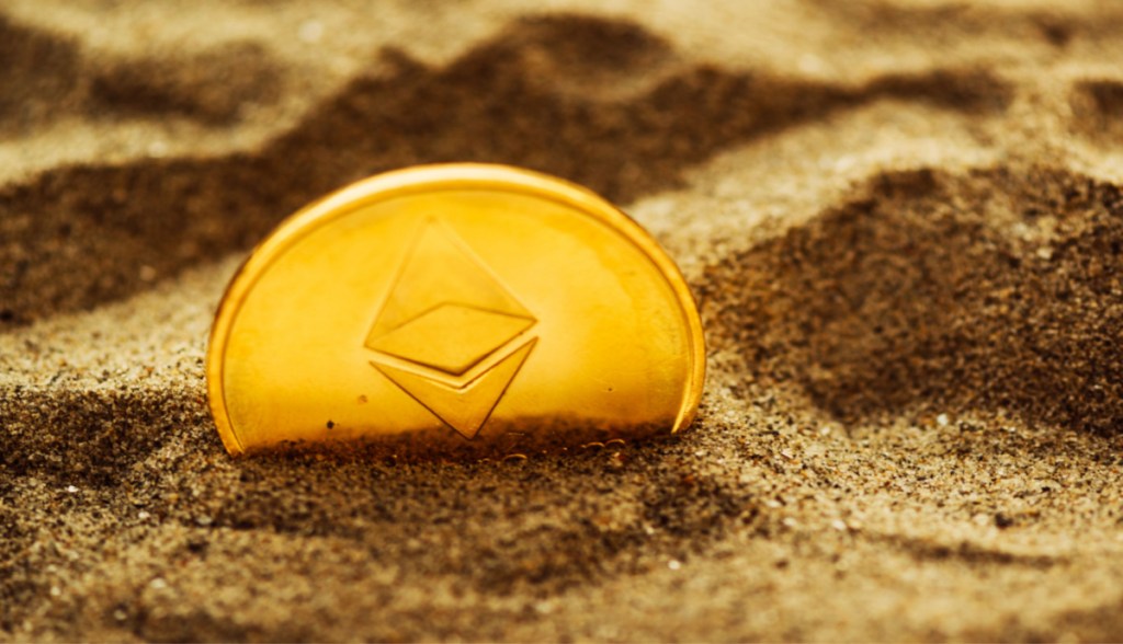 Moeda Ethereum ETH parcialmente enterrada na areia