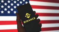 celular com logo da binance e bandeira dos EUA ao fundo