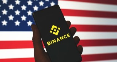 celular com logo da binance e bandeira dos EUA ao fundo