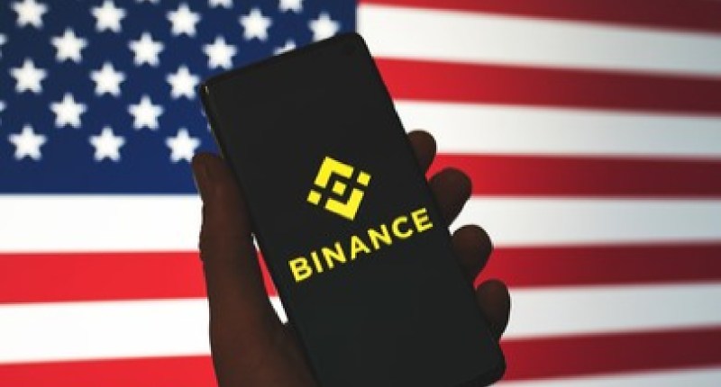 celular com logo da binance e bandeira dos EUA ao fundo