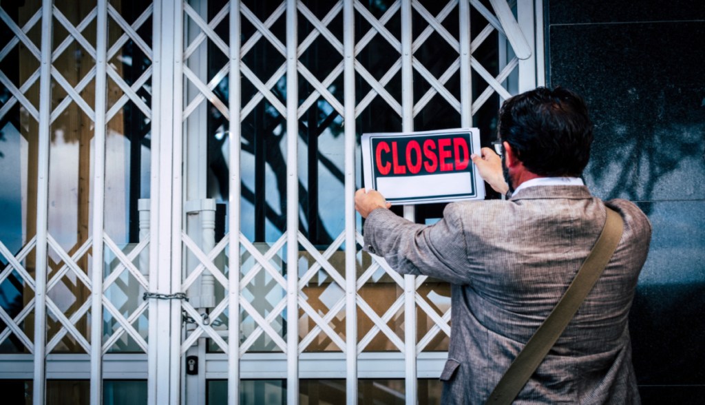 HOmem fixa placa de fechado -closed- em fachada de empresa