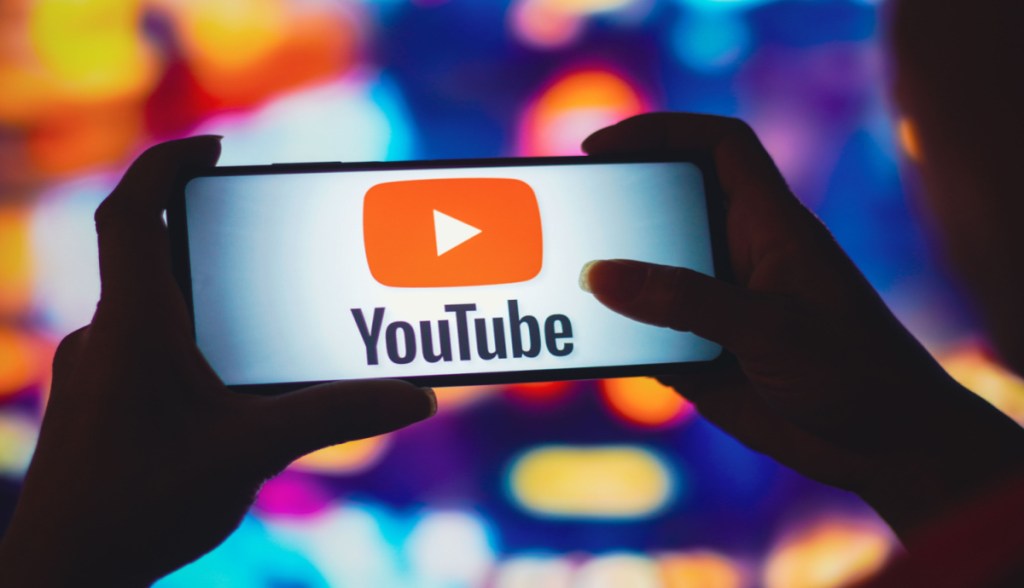 Smartphone mostra logotipo do Youtube de frente a fundo desfocado e colorido