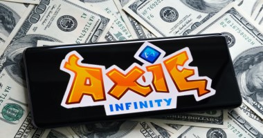 Smartphone por cima de notas de dólares mostra logo da Axie Infinity