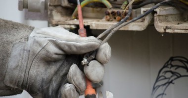 Mao com luva grossa tocando em fio de caixa de eletricidade