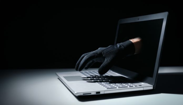 Mão de criminoso com luva preta saindo da tela de notebook em golpe financeiro na internet