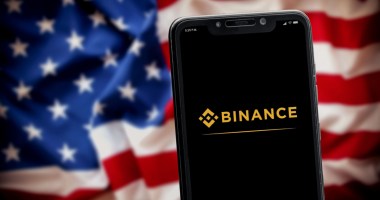 logo a binance no celular e bandeira dos EUA no fundo