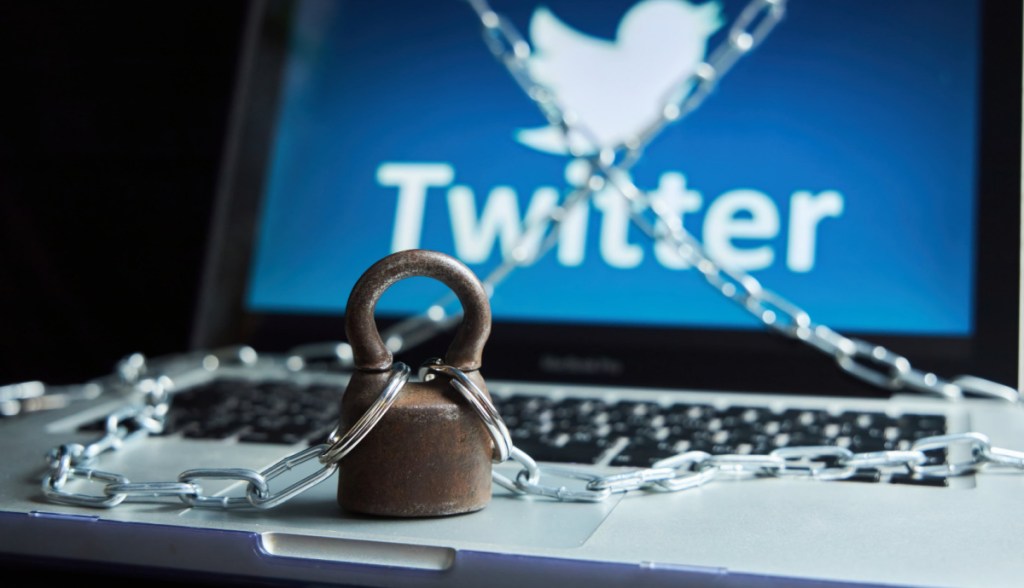 Computador com logo do Twitter em tela envolto a correntes e cadeado