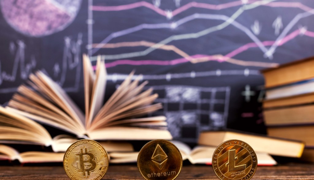 moedas de bitcoin, ethereum e litecoin à frente de quadro negor, sob mesa de sala de aula