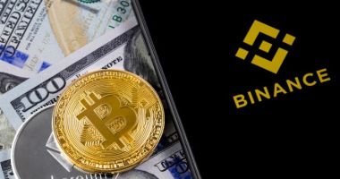 Celular com logo da Binance, moedas de Bitcoin e ETeherem em cima de notás de cem dólares