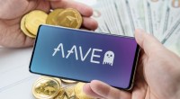 Uma mão segunra smartphone comlogomarca Aave e outra mãos critpomeodas Ethereum