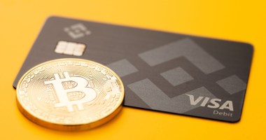 Cartão da Binance ao lado de moeda de Bitcoin