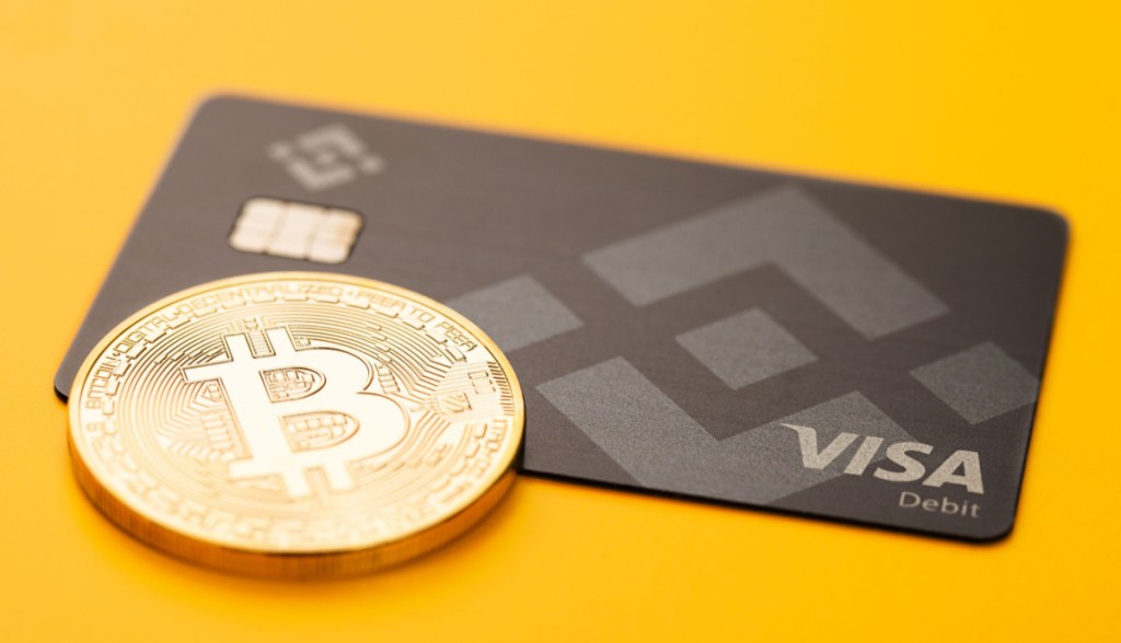 Cartão da Binance ao lado de moeda de Bitcoin