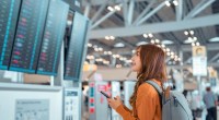 Mulher olha feliz para painel de voos em aeroporto