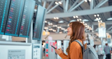 Mulher olha feliz para painel de voos em aeroporto