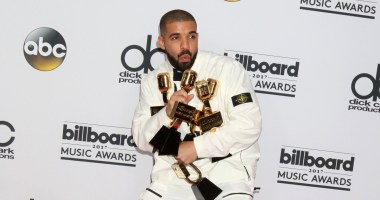 Drake, cantor e rapper, de terno branco segurando prêmios