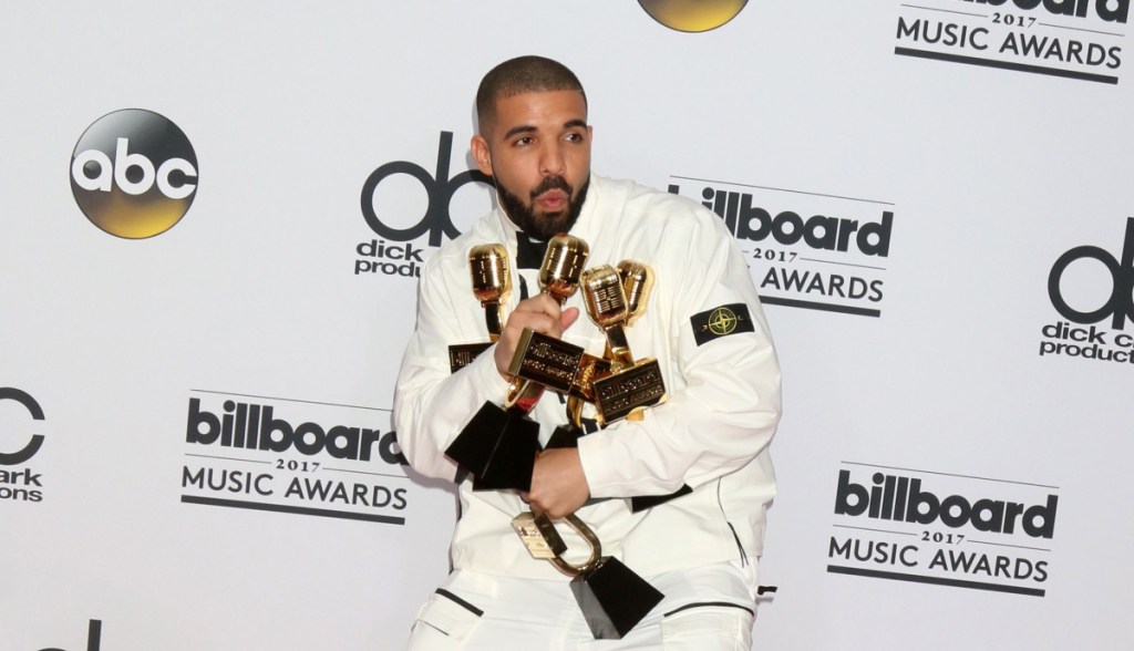 Drake, cantor e rapper, de terno branco segurando prêmios