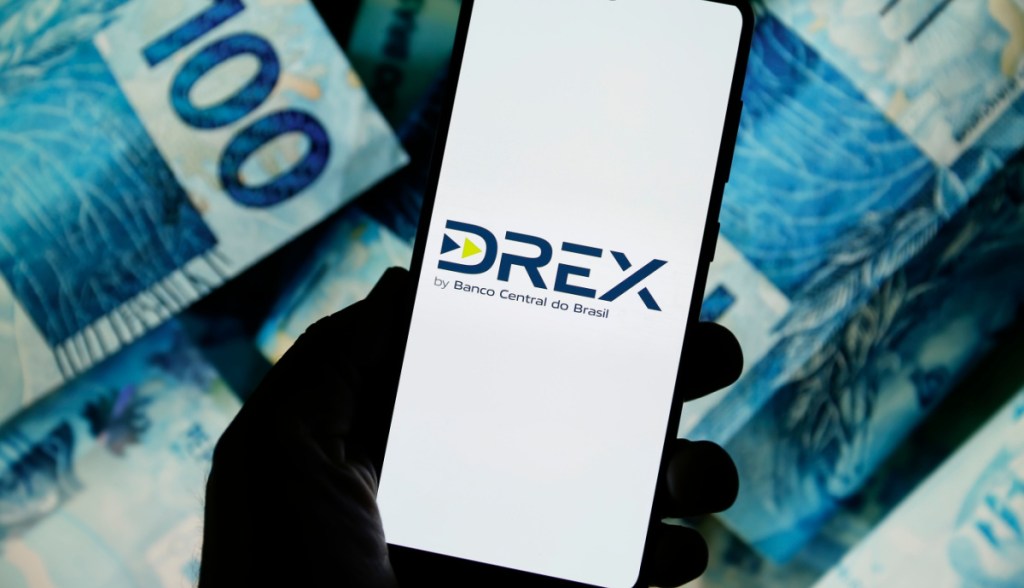 logo do drex em celular e notas de real ao fundo