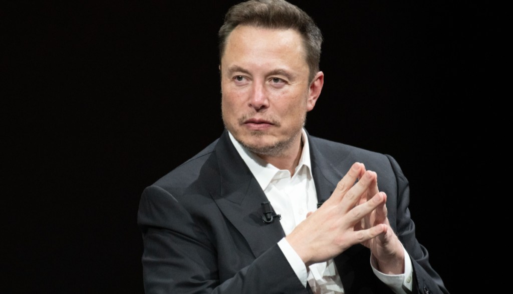 Elon Musk de paletó gesticula com as mãos