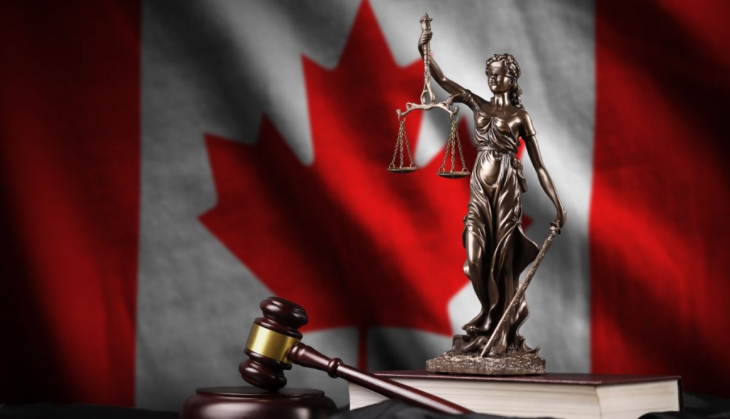 Estátua da justiça e martelo de juiz à frente de bandeira do Canadá