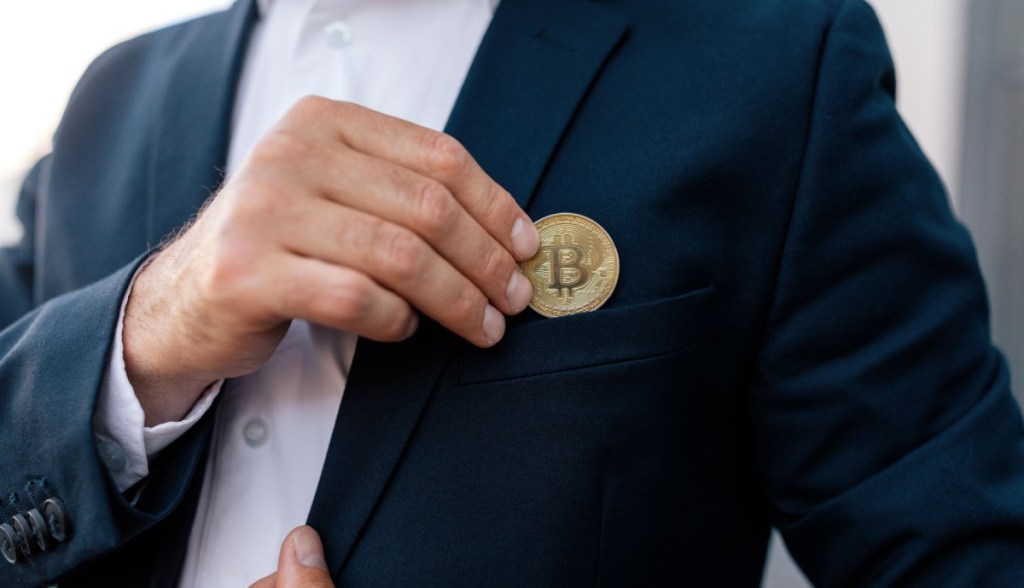 Homem de paletó tira moeda de Bitcoin do bolso