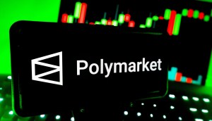 Smartphone mostra logo da plataforma de previsão Polymarjet; ao fundo, um gráfico de mercado financeiro
